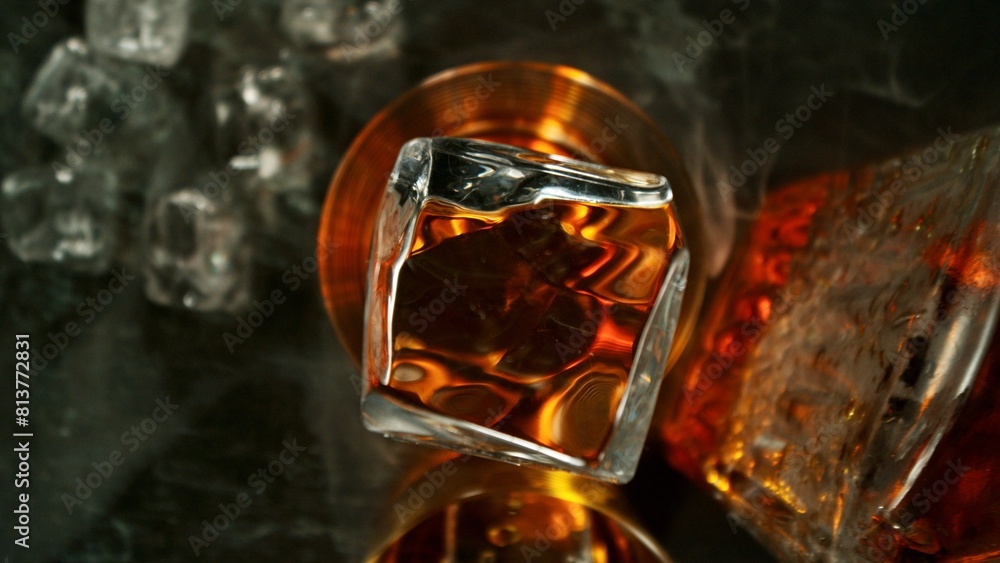 Poster closeup of ice cube falling into glass of whiskey.