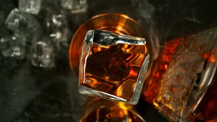 Closeup of ice cube falling into glass of whiskey.