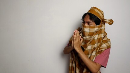 Thief from Indonesia wearing a sarong face covering and unrecognizable, poses apologizing for being...
