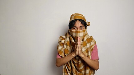 Thief from Indonesia wearing a sarong face covering and unrecognizable, poses apologizing for being...