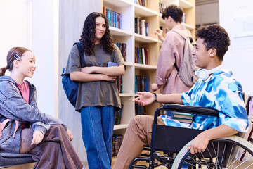 Obraz premium Side view portrait of cheerful Middle Eastern boy with disability talking to group of friends in school lounge