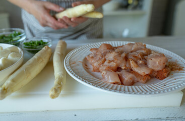 Woman preparing ingredients such as chicken and white asparagus on a cutting board for making a meal