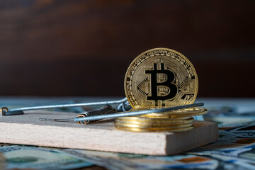 Golden cryptocurrency coins bitcoin in a mousetrap on the background of us 100 dollar bills,...