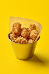Metal bucket with chicken nuggets on yellow background