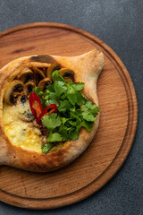 Traditional georgian khachapuri with mushrooms and cheese on a wooden board
