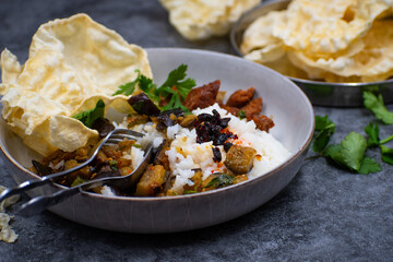A vegan Indian rice bowl with tandoori seitan,  eggplant curry, papad.