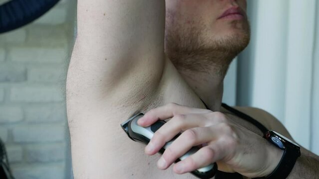 A man shaves his armpit hair, shaving with a trimmer, self-care concept.