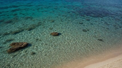 Crystal clear waters gently lap against pristine sandy shore, revealing underwater beauty of tranquil beach. Sunlight dances on surface.