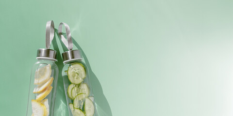 Top view two glass bottles, water drink detox with lemon and cucumber at sunlight on mint green...