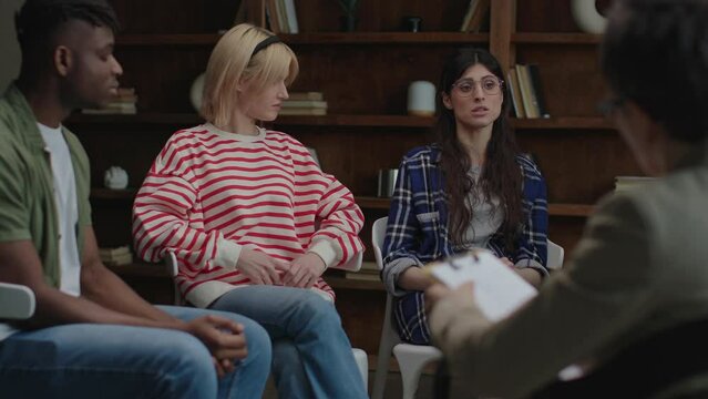 Therapy group members listen attentively in a circle as they participate in a collaborative discussion in a cozy bookshelf-lined room