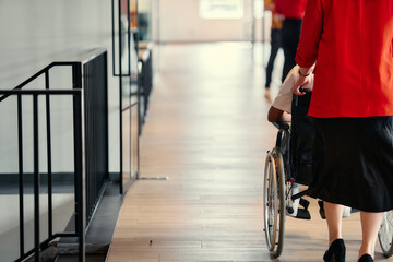 A businesswoman assists her colleague in a wheelchair as they navigate the sleek hallways of a...