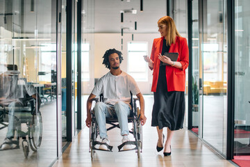 A business leader with her colleague, an African-American businessman who is a disabled person, pass by their colleagues who work in modern offices