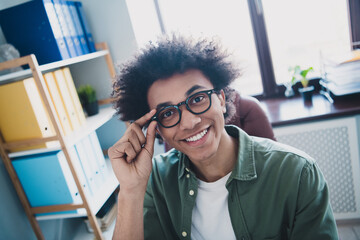 Photo of handsome cool assistant dressed khaki shirt hand arm glasses smiling indoors workstation...