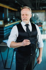 A mature businessman in a vest and white shirt is standing in a modern office.