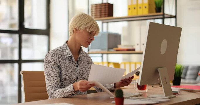 Serious woman sits in office at table and studies documents. Working time and task control in business concept