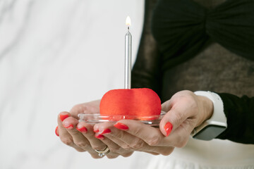 Woman holds a red cake with a birthday candle in her palms