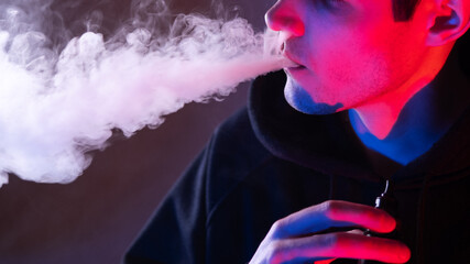 Close-up of a man exhaling steam from an electronic cigarette in close-up. Neon light .
