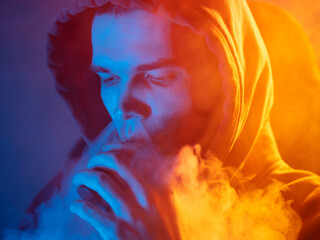 man exhaling steam from an electronic cigarette. Colored light