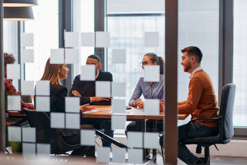 In a sleek glass office space, a team of business professionals engage in lively discussions and exchange strategic ideas, showcasing collaboration and innovation at the heart of modern corporate