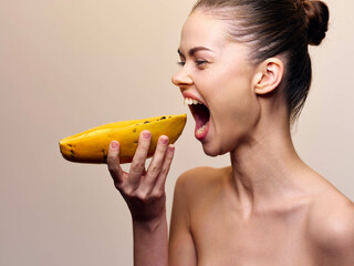 Young woman with open mouth and banana in front of her on beige background, concept of healthy...