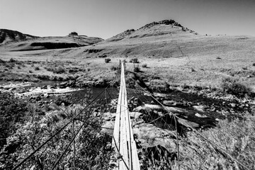 A hanging bridge crossing the Cobham river in the grasslands of the Drakensberg Mountains in South...