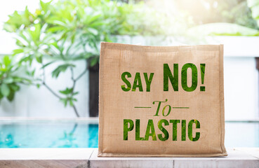 Say NO to plastic banner on hessian grocery bag over blurred green garden background, outdoor day...