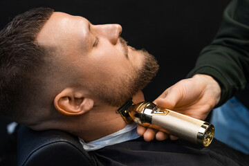 The barber uses an automatic trimmer to cut the client's beard at the barbershop