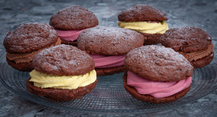 Brown cookies sandwiches with yellow and pink cream on transparent plate