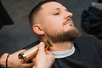 Stylist uses trimmer and comb working with client beard in barbershop closeup. Barber cuts hair on...