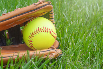 Softball in a glove in a grass field