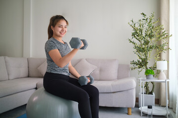 Smiling young woman exercising at home with dumbbells.