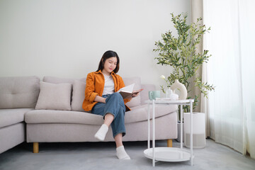 Relaxed young woman reading book in living room, spending leisure time at home.