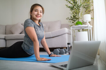 .Attractive young woman learning online yoga tutorial on laptop at home