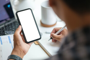 Man hands holding mobile phone while sitting at her workplace. White empty screen for your advertise design.