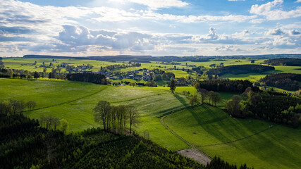 Fototapeta premium This aerial photograph captures the vast and verdant landscape of the Hautes Fagnes region, characterized by its rolling hills and vibrant green fields. The image showcases the area's natural beauty