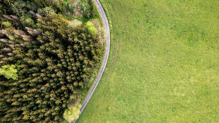 This aerial image showcases the striking contrast between a lush, vibrant green grassy field and a...