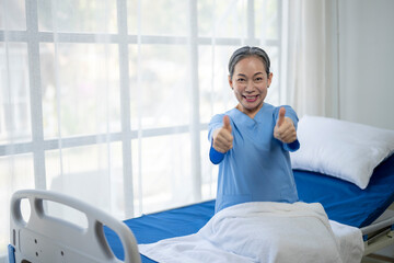 A woman in a blue scrubs is giving a thumbs up in a hospital room