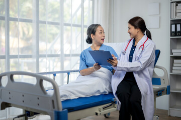 A woman in a white coat is talking to an older woman in a hospital bed