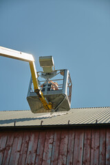 Repairing a flat roof of an agricultural building with a yellow manlift on a sunny summer day in Skaraborg Sweden