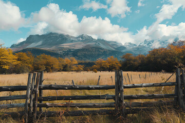 r�stica cerca de madera en un campo con �rboles de oto�o y monta�as nevadas al fondo