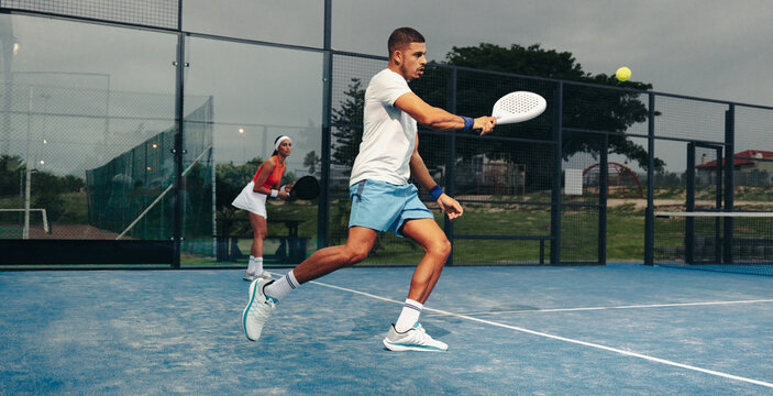Padel athlete hitting a backhand stroke during an evening match on the padel court