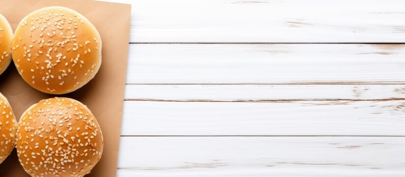 An overhead view of fresh burger buns topped with sesame seeds on a wooden board along with a blank notepad set against a white wooden background The image is captured from above providing a top view