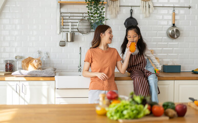 Portrait of enjoy happy love asian family mother with little asian girl preparing drinking glass of fresh juice and orange on counter in kitchen at home.Diet concept.healthy drink