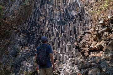 Young fit man with a backpack standing in front of the basalt monolith columns wall in a deep gorge...