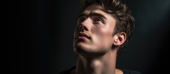 A pensive young man with a casual demeanor gazes upward in a close up portrait leaving adequate empty space in the image for copy. Copy space image. Place for adding text and design