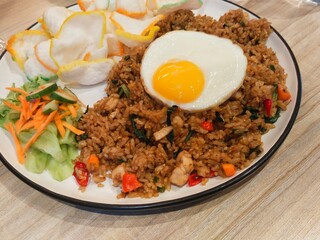 a plate of traditional fried rice with chicken, and sunny side up egg served with pickles and crackers