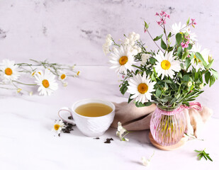 cup of herbal tea and a bouquet of chamomile flowers