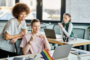 Joyous diverse businesswomen working together on project in office, pride flag.