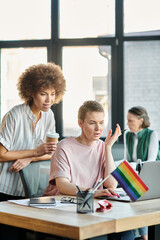 Devoted diverse businesswomen working together on project in office, pride flag.