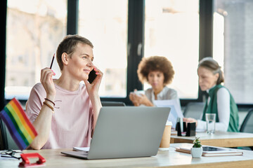 Cheerful woman engrossed in work, with a laptop in front of her, with her diverse colleagues on...